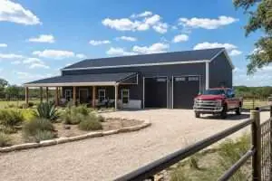 Exterior of a 40x60 black metal barndominium with attached two-bay shop and covered cedar porch in Central Texas