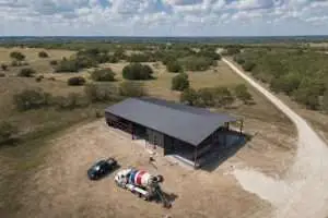 Aerial view of a barndominium under construction with red-iron steel frame on rural Texas ranch land