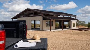 Newly framed steel barndominium on North Texas ranch land with a Texas rural lender's paperwork on a truck tailgate in the foreground